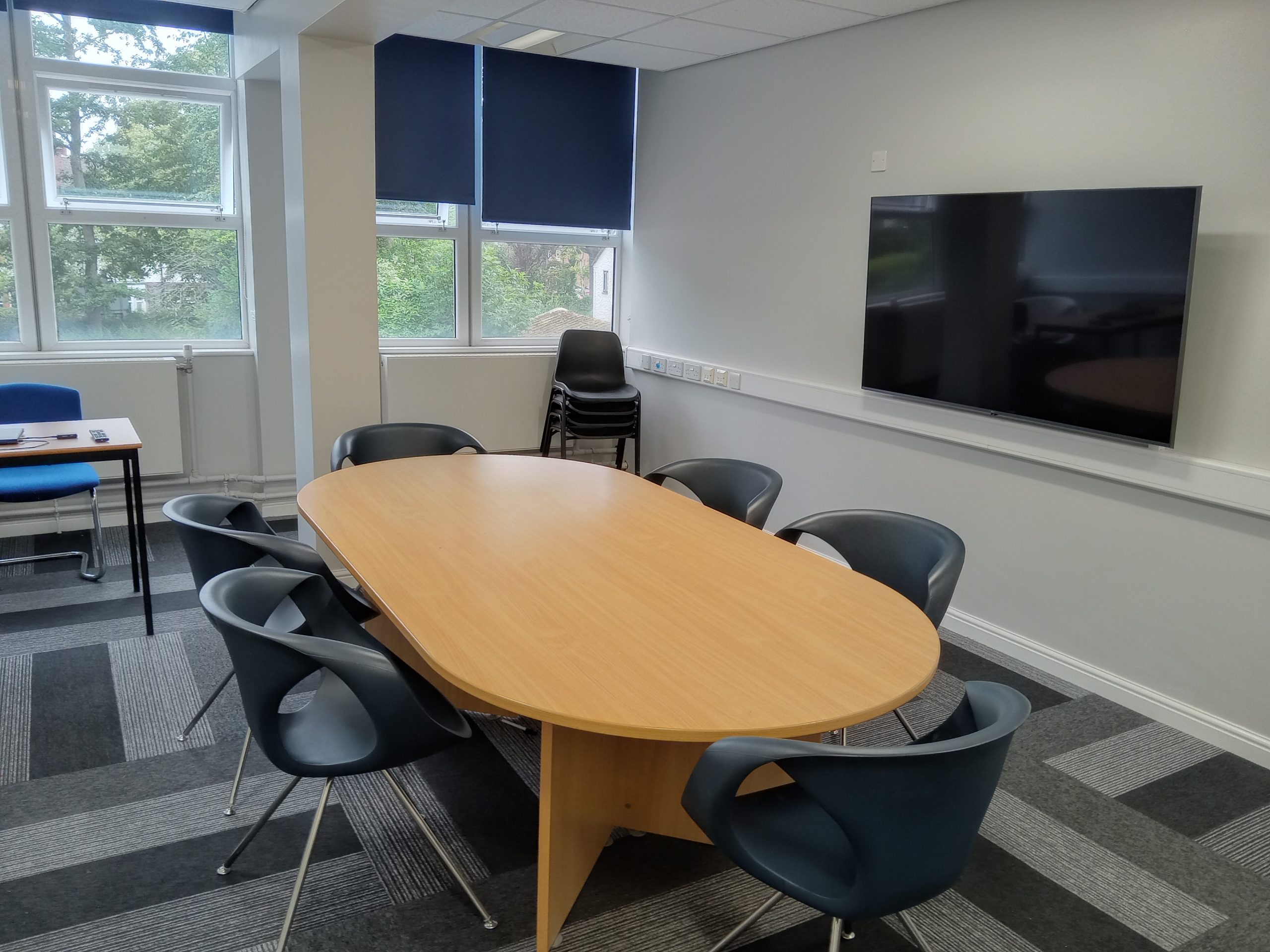 A room laid out in boardroom style, with large table and large screen display